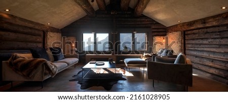 Mountain chalet living room with large sofa, two armchairs and a large window overlooking the Alps. Wooden beams and nobody inside. Royalty-Free Stock Photo #2161028905