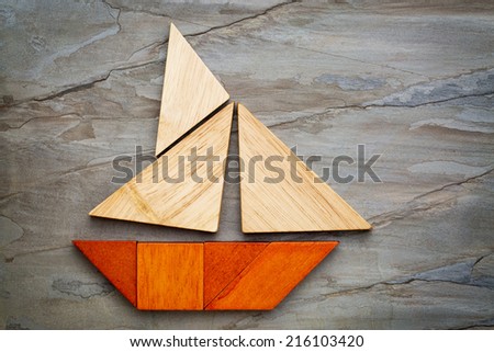 abstract picture of a sailing boat built from seven tangram wooden pieces over a slate rock background, travel or vacation concept