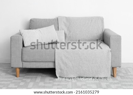 Grey sofa with pillows and plaid near light wall
