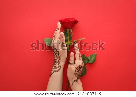 Female hands with beautiful henna tattoo and rose flower on color background, closeup