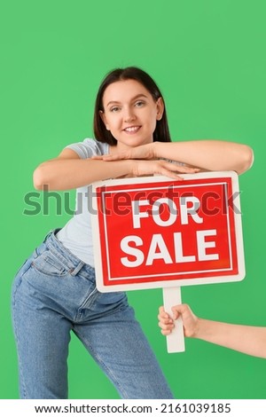 Young women with FOR SALE sign on green background