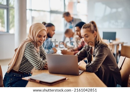 Happy Muslim student and her college friend cooperating while  using laptop during a class at college classroom.  Royalty-Free Stock Photo #2161042851