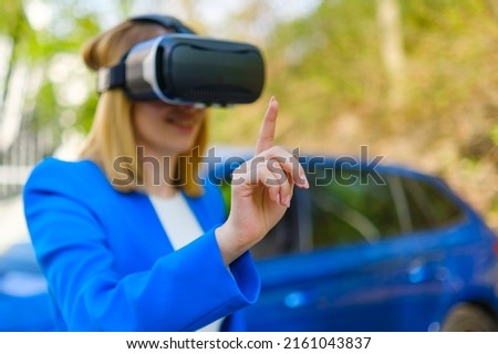 Business woman using VR goggles, moving her head touching the simulation screen with blue car on the background