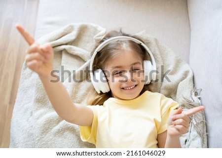 Little girl listening to music enjoying the song on the sofa in the living room and wearing headphones at home.