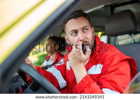 handsome young male paramedic talking by portable radio while sitting in ambulance Royalty-Free Stock Photo #2161049341
