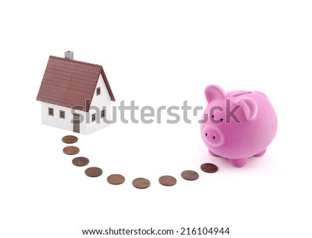 Saving for a house. Piggy bank with coins and house miniature.