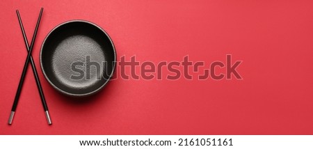 Chinese bowl with chopsticks on red background with space for text