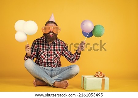 happy handsome bearded guy with unshaven face and stylish hairdo wear casual clothes holding present and party balloons, birthday holiday