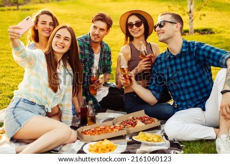 Happy friends have a picnic in the city park outdoors. Young people drink drinks and eat pizza and laugh in the street while sitting on a ravine