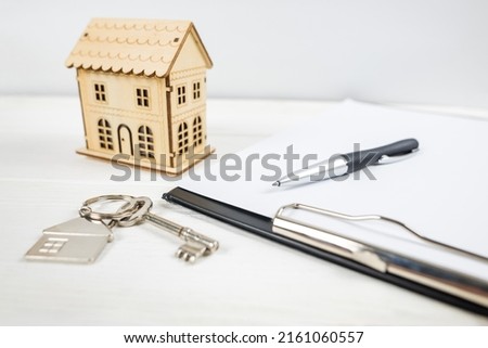 Close-up of wooden house, keys, clipboard and pen. Real Estate Concept. Model house, keys, blank business card, pen and calculator on wooden table. 