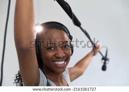 Black Woman Smiling Working on Movie Set as Audio Person Holding Boom Pole Microphone. She is a Video Production Crew Member