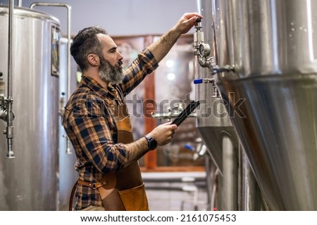 Man is working at craft beer factory. He is operating machinery in brewery. Small family business, production of craft beer. Royalty-Free Stock Photo #2161075453