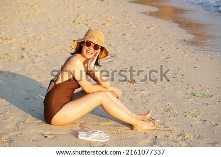 Asian young girl wearing straw hat, sunglasses and brown swimwear happy on the beach with copy space. Portrait. Summer activity.