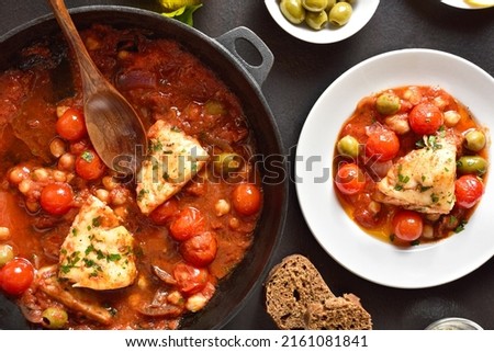Cod stew with chickpeas, cherry tomatoes and olives over dark stone background. Top view, flat lay
