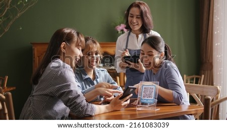 Adult waiter staff casual apron SME owner enjoy work listen to young asia people smile fun talk look at smart QR code on mobile app eat vegan meal after reopen coffee shop food drink inside cafe bar. Royalty-Free Stock Photo #2161083039