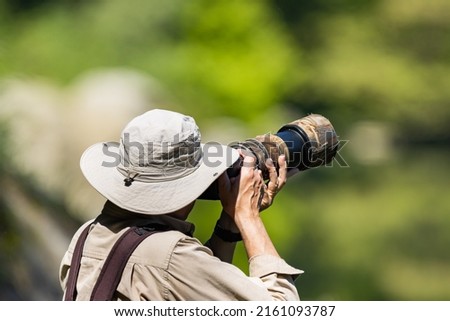 Wildlife photographer using a telephoto lens with camouflage coating.