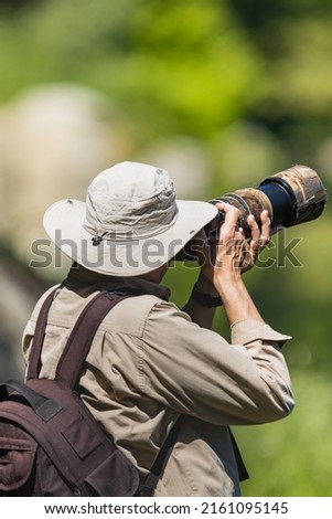 Wildlife photographer using a telephoto lens with camouflage coating. Royalty-Free Stock Photo #2161095145