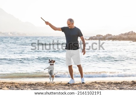 60-years old athletic man playing with small cute jumping dog jack russell terrier by the sea. Royalty-Free Stock Photo #2161102191