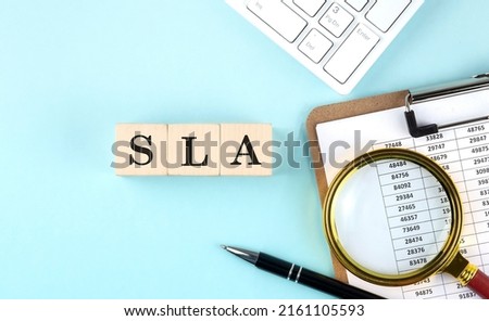 SLA - Service Level Agreement word on a wooden cubes on a blue background with chart and keyboard