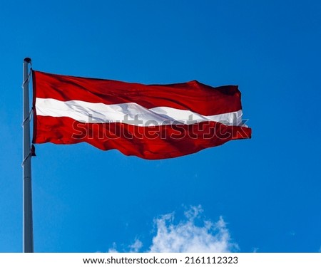 Latvian flag in the wind waving in the blue sky