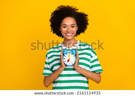Photo of nice millennial lady hold clock wear striped t-shirt isolated on yellow color background