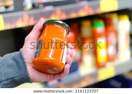 male hand holds jar of sauce on blurred background, row of shelves with groceries in supermarket, concept of marketing, prices for consumer goods, consumer basket, rising prices for essential goods