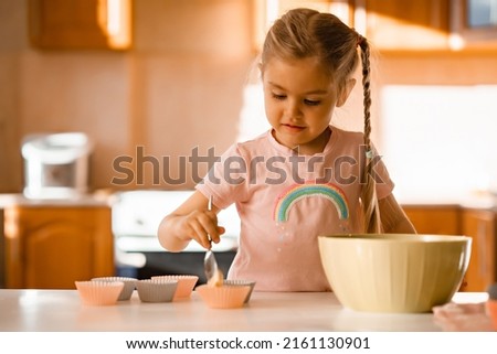 Cute smiling little blonde girl cooking dough in kitchen at home. High quality photo