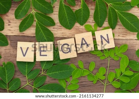 green moringa leaf background with vegan writing using wooden blocks