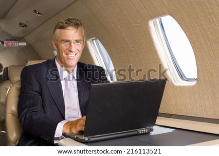 Businessman using laptop computer on aeroplane, smiling, portrait