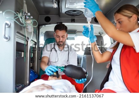View from inside ambulance of uniformed emergency services workers caring for patient on stretcher during coronavirus pandemic. Royalty-Free Stock Photo #2161137067