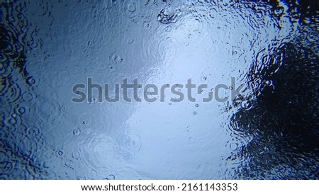 View from under the water to the sky and rain. Drops fall on the surface of the water create water circles. Gray clouds and blue sky are visible. Dark green highlights of trees. An unusual look Royalty-Free Stock Photo #2161143353