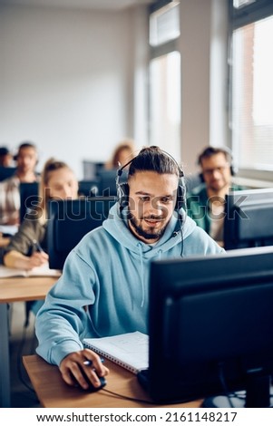 Male student learning on desktop PC during computer class at college classroom.