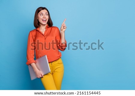 Photo of young curious girl look indicate finger empty space promo select direct hold laptop isolated over blue color background
