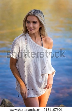 A gorgeous blonde bikini model poses outdoors near a lake while enjoying the summer weather.