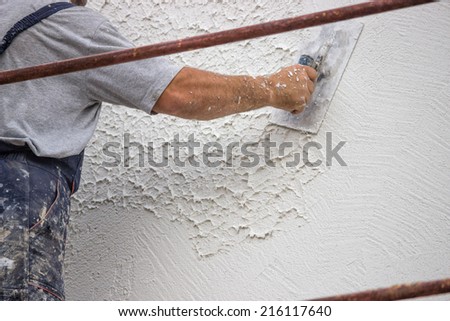 Decorative plaster applied on the surface by a steel trowel. White cement based decorative top coat plaster resistant on outside whether conditions. Selective focus. Royalty-Free Stock Photo #216117640