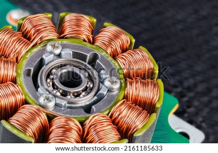 Electric engine stator with coils copper wire winding or ball bearing on green PCB detail. Closeup of step motor inductors or metal ferromagnetic sheets from laser printer machine on blurry black net. Royalty-Free Stock Photo #2161185633