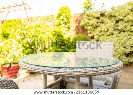 Shallow focus of the corner of a natural woven garden table, seen with its safety glass. Located on a patio area.