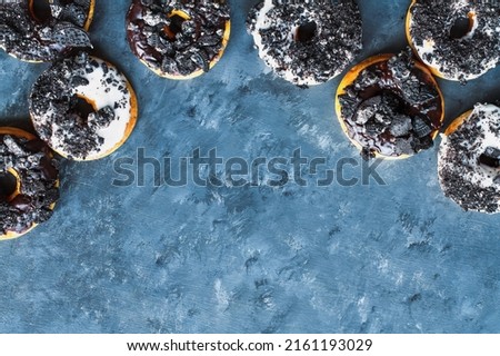 Flatlay of dark and white chocolate frosted donuts with crumbled creme filled cookies over a blue textured painted background.