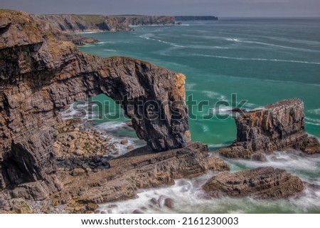 The Green Bridge of Wales is a dramatic natural rock arch on the southwest coast of Pembrokeshire.  Royalty-Free Stock Photo #2161230003