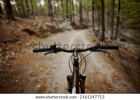 Mountain bike handlebar viewed from the first-person perspective. visible bicycle frame and bicycle accessories on the handlebar and the forest trai. Concept of spending time outdoors while bikeriding Royalty-Free Stock Photo #2161247713
