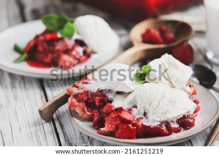Sweet homemade strawberry cobbler or Sonker with French vanilla ice cream over a rustic white wood table. Extreme selective focus with blurred background.