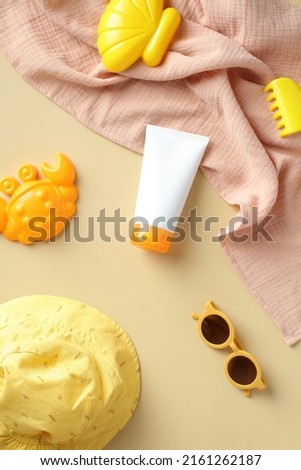 Sun protection cream tube for babies and children with panama hat, towel, sunglasses, sandbox toys on beige background. Sunscreen lotion for kids. Flat lay, top view.