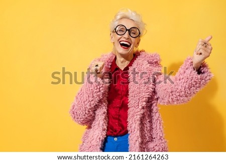 Happy and playful mature woman dancing, smiling and having fun. Photo of elderly woman above 70 years old in stylish outfit on yellow background