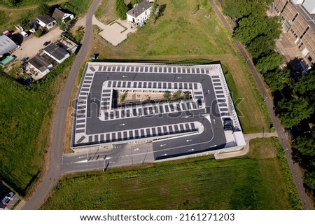 Slanted top down aerial view with a single car parked in graphic outline parking lot with arrows and spots marked in the dark asphalt on elevated roof top