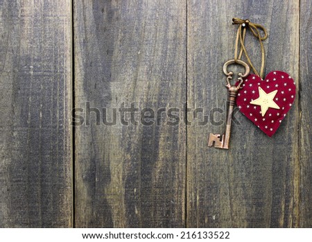 Bronze skeleton house key and red country fabric heart with stars hanging on antique  old rustic wood door; Valentines Day, real estate and home concept background with wooden copy space