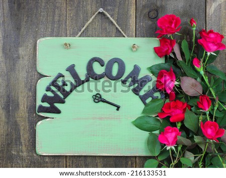 Green welcome sign with key and flower border of red roses hanging on rustic wood door