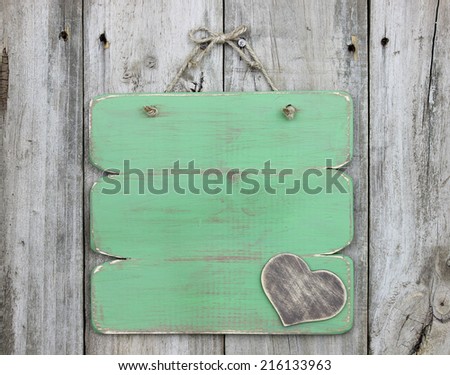 Blank green sign with wooden heart hanging on old weathered wood door