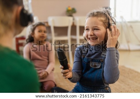 Little girls with headphones and microphone taking an interview, having fun and playing at home. Royalty-Free Stock Photo #2161343775
