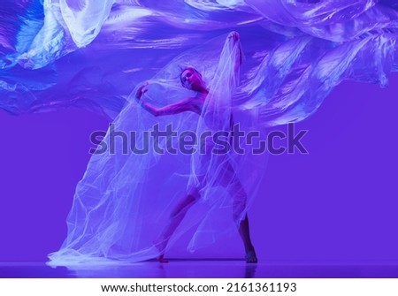 Portrait of beautiful flexible woman, ballerina dancing with cloth on purple background in neon. The grace, artist, movement, action and motion concept. Looks weightless, flexible. Fashion, style.