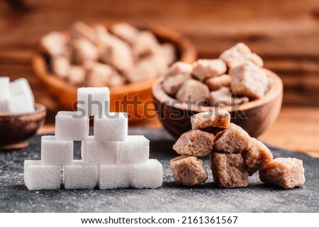 Bowl and scoop with white sand and lump white sugar on wooden background. Brown sugar cube. Make unhealthy nutrition, obesity, diabetes, dental care and much more.